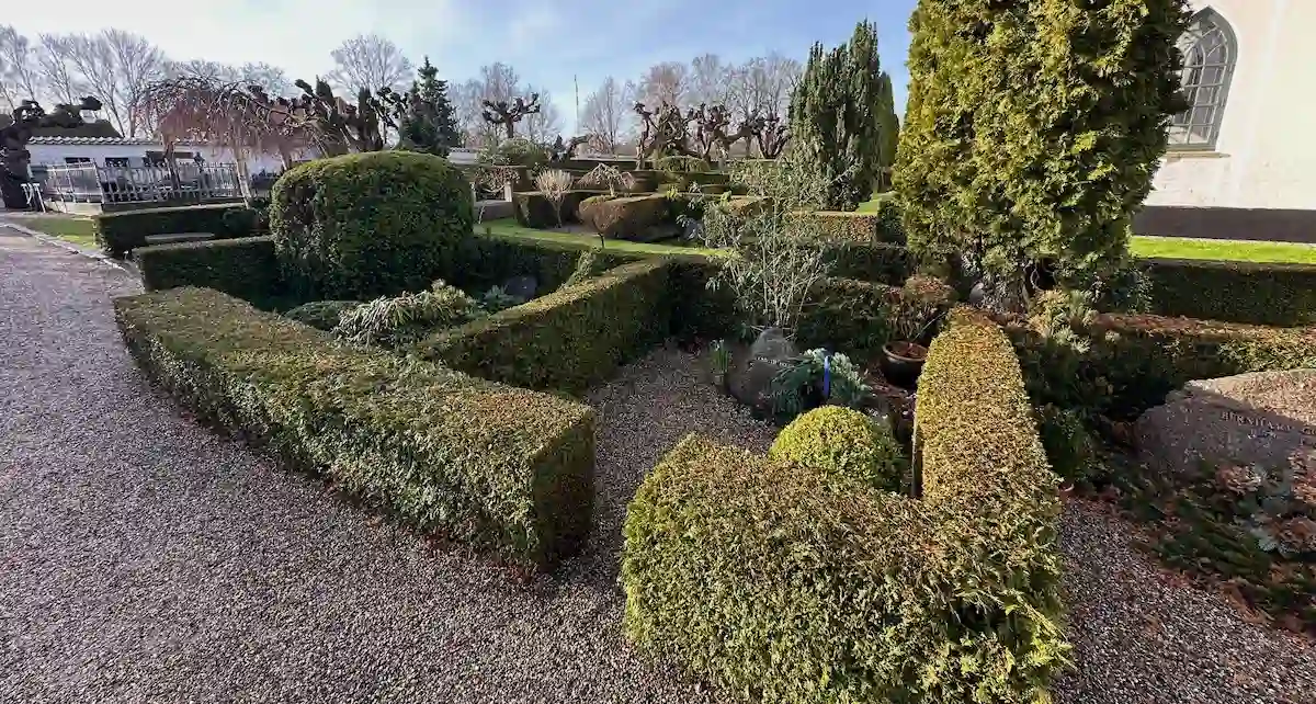 Kistegravsted med gravsten, beplantning og hække på dansk kirkegård