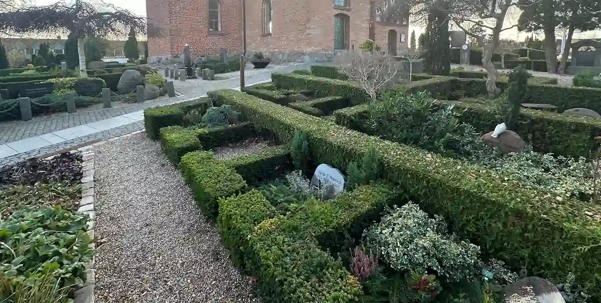 Urnegravsted med gravsten, hæk og beplantning på kirkegård